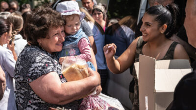 Ukrainian woman holding Ukrainian toddler girl while receiving Bible and humanitarian aid.